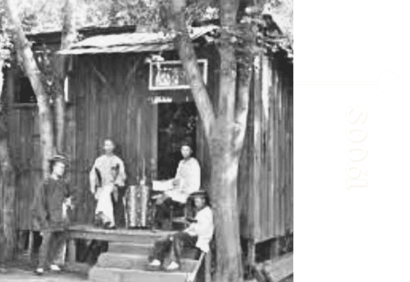 Group of people posing outside a wooden structure in the early 1900s.