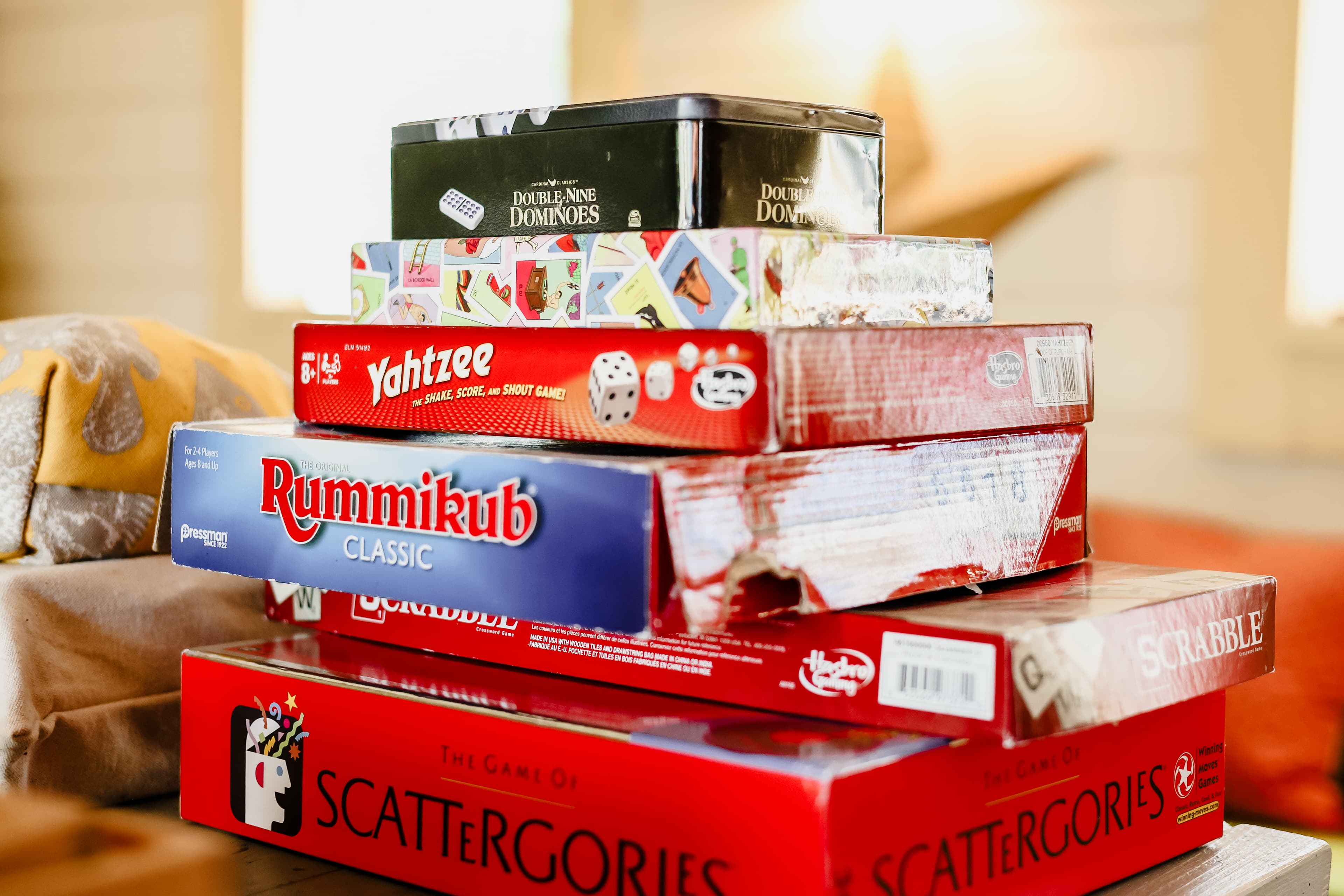 A stack of various board games including Yahtzee, Rummikub, Scrabble, and Scattergories.