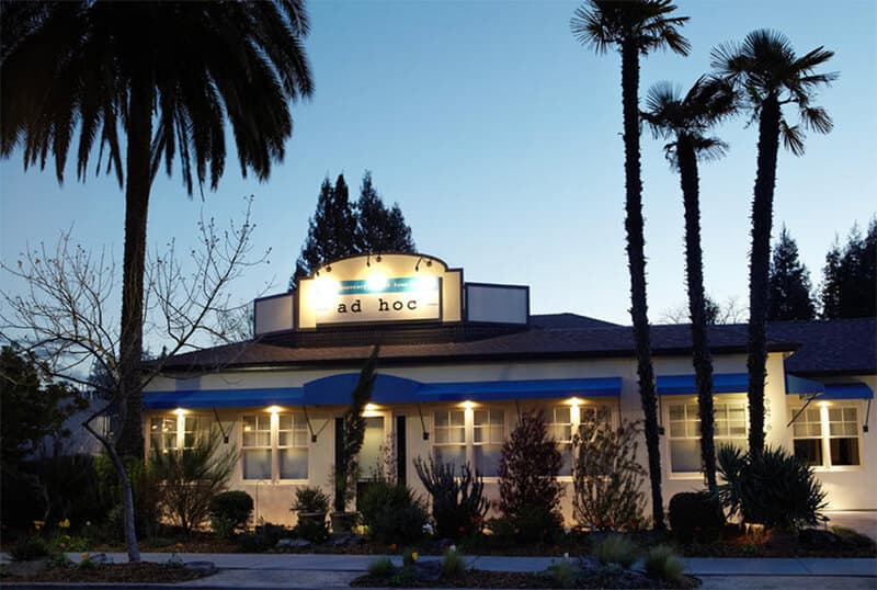 A building with the sign "ad hoc" surrounded by palm trees at dusk. A building with the sign "ad hoc" surrounded by palm trees at dusk.