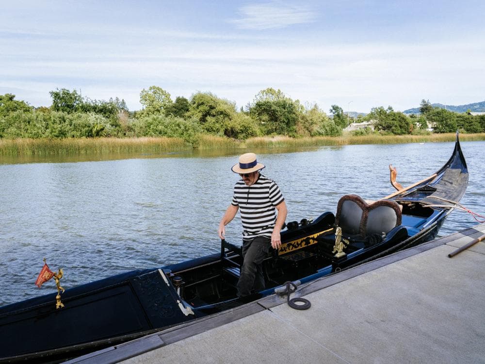 A gondolier in a striped shirt prepares a gondola by the water.