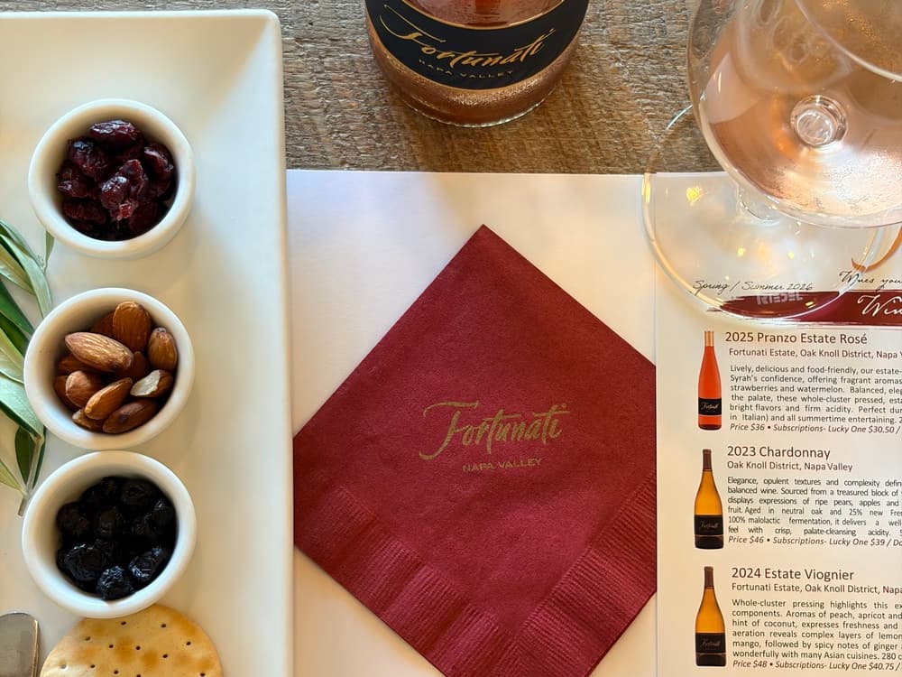 A tasting setting featuring a selection of nuts and dried fruits, a wine glass, a menu, and a branded napkin.