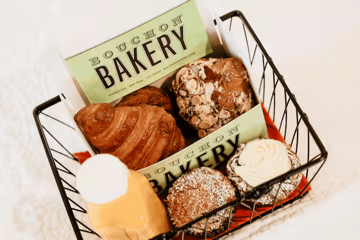 A wire basket filled with assorted baked goods and a bottle of juice, featuring Bouchon Bakery branding.