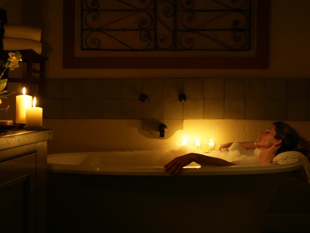 A woman relaxes in a dimly lit bathtub surrounded by candles and bubbles.