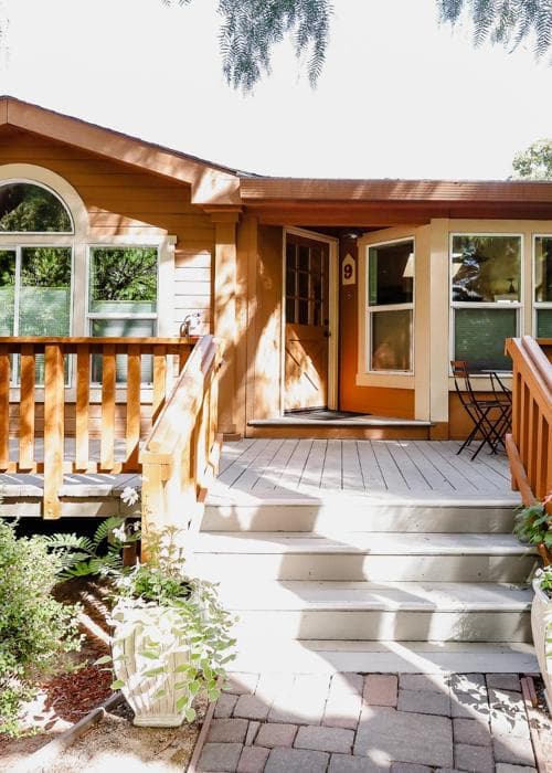 Front entrance of a cozy wooden house with a porch and steps leading up to the door.