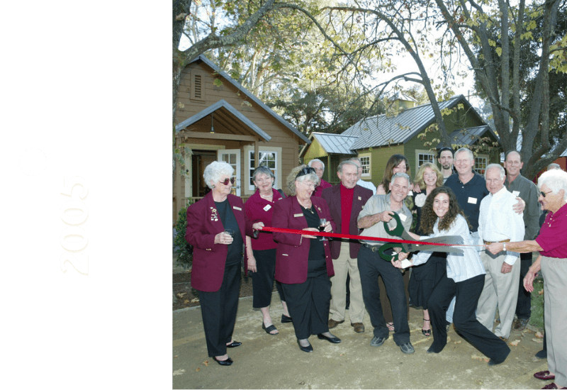 A group of people gathers outdoors to celebrate a ribbon-cutting ceremony in front of newly built houses in 2005.
