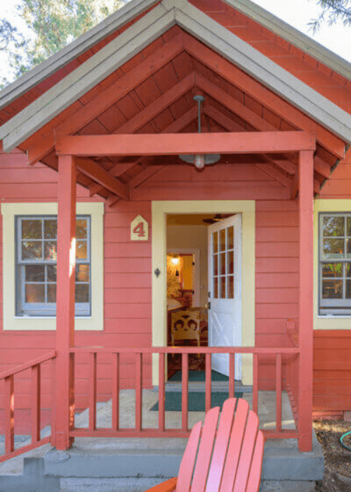 Front entrance of a red cottage with a welcoming porch and an open door.