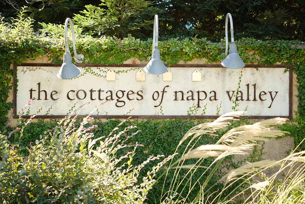 Sign for "the cottages of napa valley" surrounded by greenery and decorative lighting.