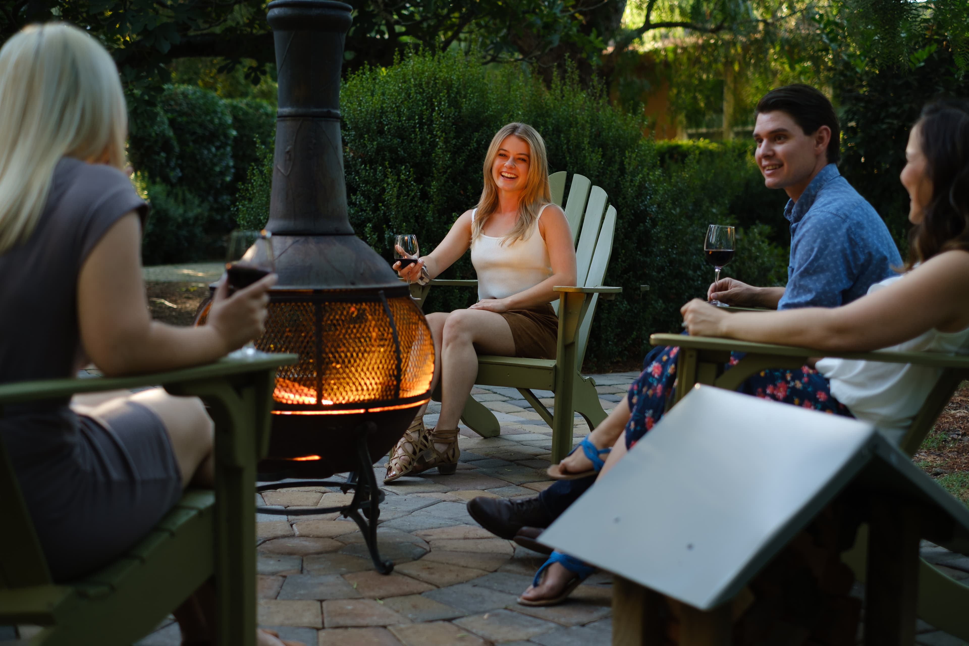A group of four friends enjoys wine and conversation around a cozy outdoor heater.